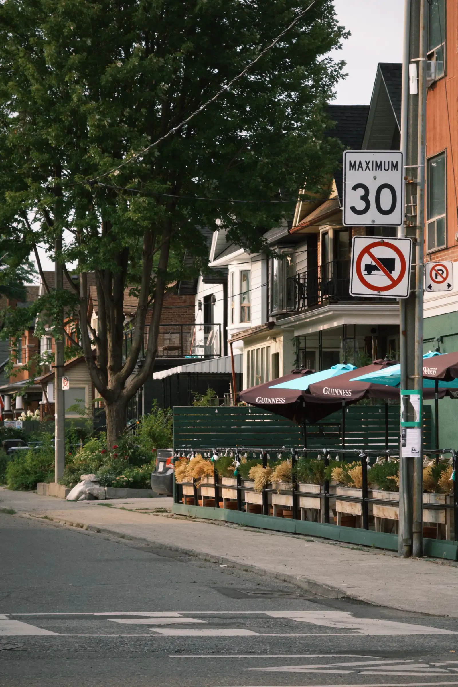 A leafy Toronto street with a café patio and red umbrellas in front of brick houses